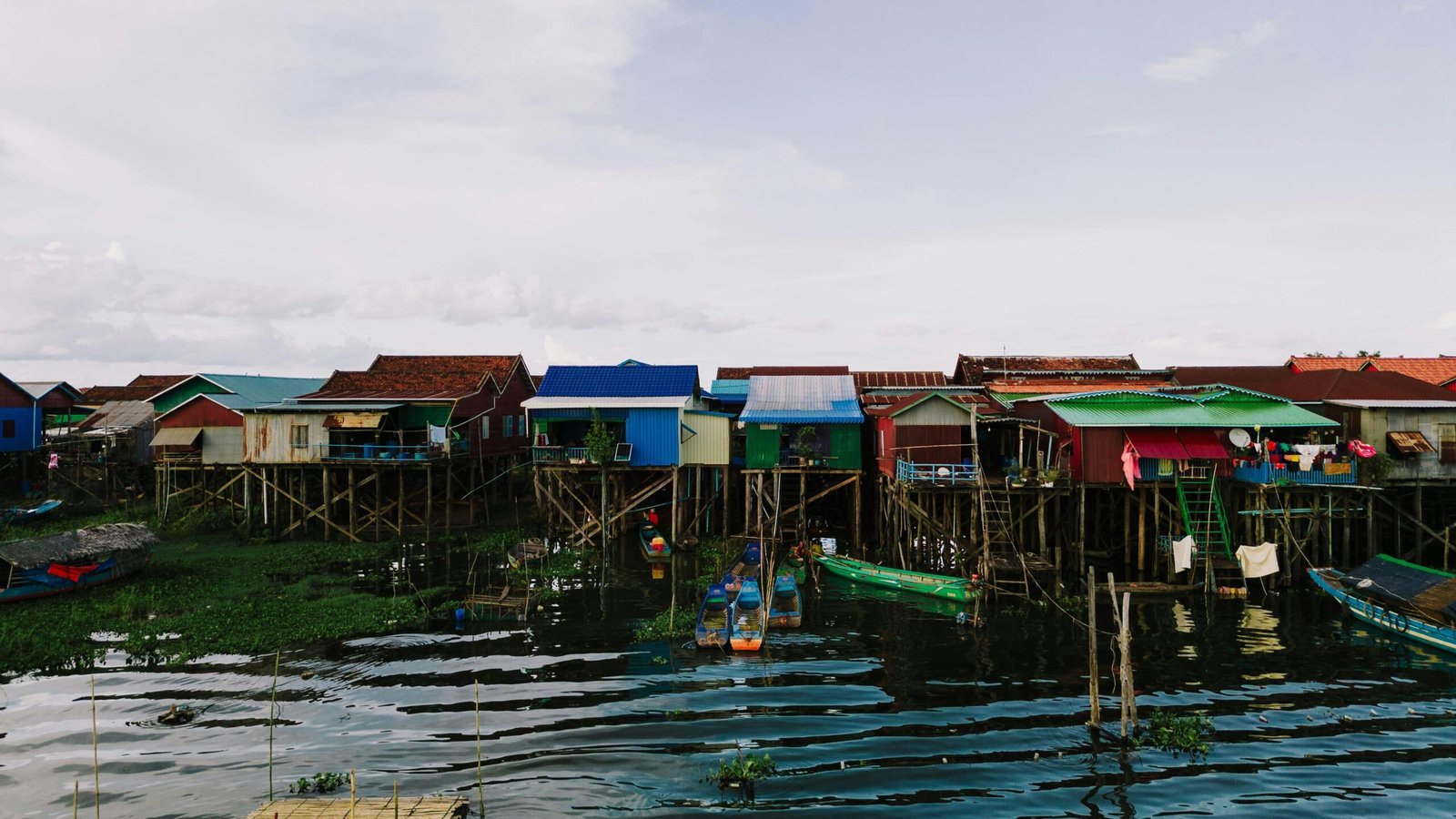 Colorful stilt houses line the shore of Kampong Khleang, reflecting in the water below.